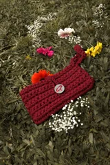 Bolso de mano tejido a crochet en trapillo grueso color verde oscuro, con un botón metálico grande y redondo con el logo de la marca CAPER en rojo.