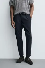 Pantalón de corte slim fit y color negro, confeccionado en tejido elástico. Cuenta con cintura elástica, trabillas, bolsillos frontales y cierre con cremallera y botón.