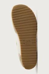 Zapatilla deportiva estilo barefoot, color marrón, con diseño de paneles en combinación de materiales y detalles en serraje. Cuenta con puntera redondeada y ancha, cordones en color crema y suela fina de goma flexible en contraste.