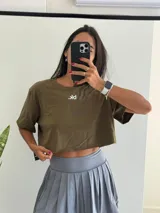 Remera corta (crop top) de manga corta y cuello redondo, color verde militar, con un pequeño logo blanco bordado en el pecho.