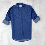 Camisa de jean azul marino, con cuello mao, manga larga con puños abotonados, cierre frontal con botones y bolsillo en el pecho con detalle de rotura.
