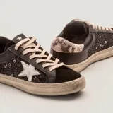 Zapatillas urbanas de cuero vacuno negro con aplique de estrella de cuero blanco, caña de glitter negro y cordones de algodón encerados color topo. Suela de caucho y plantilla de goma eva de 17 mm.
