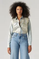 Camisa de estilo western con acabado metalizado brillante en tono azul claro y plateado. Presenta cuello clásico, cierre frontal con botones a presión, dos bolsillos en el pecho con solapa y mangas largas con puños abotonados.