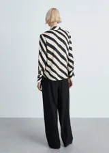 Camisa de corte recto y ajuste regular, confeccionada en tejido satinado fluido y ligero. Presenta un diseño estampado con rayas diagonales en tonos beige y negro, cuello camisero clásico, cierre frontal de botones y mangas largas con puños abotonados.