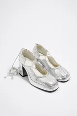 Zapatos de tacón plateados con plataforma, punta cuadrada, tiras cruzadas y cordones para atar al tobillo.