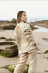 Camisa de lino color marrón rojizo, con cuello clásico y botones frontales blancos. Presenta pliegues verticales en el torso y mangas largas abullonadas con frunces elásticos en los puños.