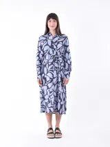 Vestido camisero midi de manga larga, con cuello y botones frontales, ajustado a la cintura con un lazo. Presenta un estampado abstracto en tonos azul claro y azul oscuro/negro.