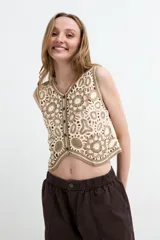 Chaleco crop de crochet en tonos beige y tostado, con diseño calado de motivos florales, escote en V y cierre frontal de botones.