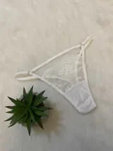 Tanga tipo colaless de encaje blanco con tiras laterales regulables y refuerzo de algodón en la entrepierna.