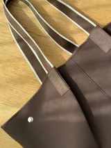 Bolso tipo tote de neopreno en color verde oliva, con correas de hombro en color rojo y detalles en blanco. Cuenta con broches imantados laterales para ajustar su forma y un bolsillo interno de red.