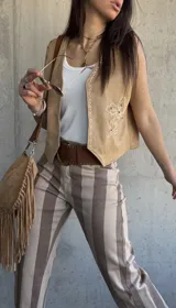 Chaleco de gamuza color beige, con bordados florales en contraste, detalles de tachas metálicas en los bordes y diseño frontal abierto.