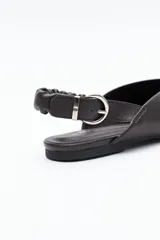 Zapato destalonado de punta fina, color negro, con base baja y tira trasera elástica con hebilla metálica ajustable. Diseño minimalista.