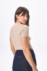 Top corto de tejido de punto color beige, con cuello polo, mangas cortas y cierre frontal con cordones.