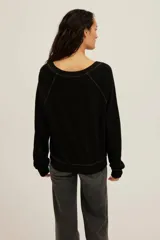 Sweatshirt Cambridge de felpa ligera en color negro, con corte holgado y escote en V pronunciado con ribetes en contraste. Presenta mangas largas con puños ajustados y costuras visibles.