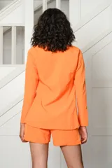 Conjunto de tres piezas color naranja, compuesto por un blazer de corte sastre, un top tipo bandeau fruncido y un short de tiro alto con dobladillo en las piernas.