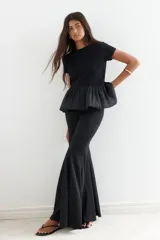 Top negro de manga corta y cuello redondo. La parte superior es de tejido liso y ajustado, mientras que la parte inferior es un bajo globo con textura plisada y semitransparente.