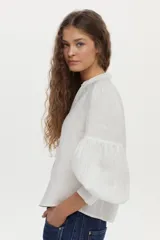 Camisa de lino color beige, con escote en V, cuello mao y mangas abullonadas tres cuartos. Cuenta con cierre frontal de botones y tiras ajustables para atar en la cintura.