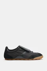 Championes deportivos de estilo minimalista, confeccionados en una combinación de materiales textiles y sintéticos con textura. Presentan una lengüeta superpuesta con cierre de gancho, cordones ocultos, punta redonda y suela plana de goma color caramelo.