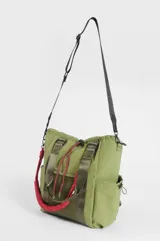 Cartera tipo shopper color marrón, con compartimento principal con cierre, bolsillos laterales, bolsillo frontal de red y cordones decorativos en color rosado. Cuenta con correas dobles de hombro y una correa extraíble de cuerda trenzada en color rosado y blanco.