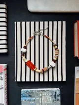 Collar corto de diseño artesanal, compuesto por una gran variedad de cuentas de piedra, madera y cerámica en tonos tierra, rojo y blanco, con cierre metálico ajustable.