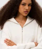 Campera cropped de tricot color blanco off-white, confeccionada en algodón con textura acanalada. Presenta cuello amplio con cierre metálico frontal, mangas largas con puños acanalados y cintura marcada con banda ancha.