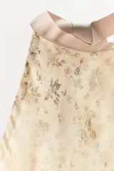 Top halter de tejido ligero con estampado floral en tonos tierra sobre fondo beige. Presenta diseño sin mangas, espalda descubierta y cierre con lazadas en el cuello y la espalda, con un bajo asimétrico.