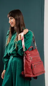 Mochila de símil cuero color marrón con apertura superior y tres bolsillos frontales con cierres metálicos. Cuenta con bolsillos laterales y una correa de galón con diseño geométrico, regulable y extraíble, que permite su uso como bandolera.