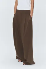 Pantalón de tiro medio color marrón, con pinzas en el delantero, perneras anchas de corte recto y trabillas para cinturón. Cuenta con bolsillos laterales y traseros, y cierre frontal con cremallera y botón.