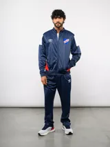 Conjunto deportivo Umbro del Club Nacional de Football, compuesto por una campera con cierre frontal y un pantalón a juego. Ambas piezas son de color azul marino con detalles en blanco y rojo, presentando el escudo del club y el logo de la marca.