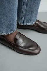 Mocasín de vestir en piel color marrón oscuro, con detalle de antifaz en el empeine, horma redonda y suela de goma Vibram.