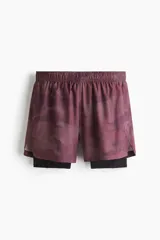 Short deportivo de doble capa, con calza interior. El short exterior es de color borgoña con un estampado sutil de puntos en forma de camuflaje. Posee cintura elástica con cordón oculto y aberturas laterales. La calza interior es negra.