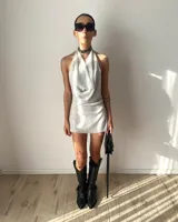 Vestido corto de tela brillante plateada con cuello drapeado, diseño halter y espalda descubierta.