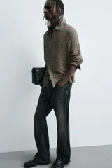 Camisa de hombre de corte relaxed fit, color marrón oscuro, con cuello solapa, manga larga terminada en puño con botón y cierre frontal de botonadura. El tejido presenta una textura acolchada o gofrada con patrón de pequeños cuadros.