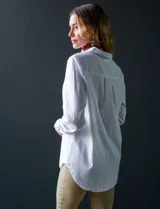 Camisa blanca de manga larga, corte holgado, con cuello con solapa, abertura central con botones y bolsillo aplicado en el pecho.