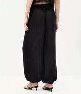 Pantalón balloon de crepé negro, de corte amplio y cintura elástica, con detalles de encaje en los laterales y puños inferiores elastizados.