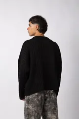Sweater negro de calce relajado con diseño de textura combinada, presentando un lado liso y otro con tejido de ochos. Cuenta con cuello redondo y una etiqueta decorativa en el frente.
