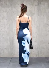 Vestido largo de corte ajustado, confeccionado en tela elastizada de color azul oscuro con un estampado floral abstracto en tonos blancos que recorre el lateral de la prenda. Presenta escote redondo y breteles finos.