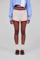 Short deportivo de tejido polar color crema con ribete naranja, cintura elástica marrón y logo bordado en el frente.