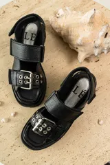 Sandalias negras de cuero con diseño de plataforma dentada, tiras ajustables con hebillas metálicas y detalle de tachas plateadas en el lateral de la suela.
