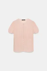 Top de georgette semitransparente color rosado, con cuello redondo, mangas cortas abullonadas y cierre frontal con botones. Presenta detalles de alforzas en la parte inferior.