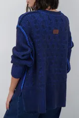 Buzo reversible de tejido de punto con diseño de trenzas, cuello redondo y mangas largas. Presenta una combinación de colores en contraste, con un lado en violeta y el otro en marrón oscuro.