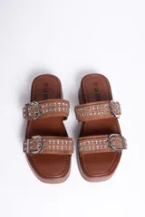 Sandalias de plataforma color marrón camel, con dos tiras en el empeine decoradas con hebillas metálicas plateadas y tachas. Suela plana y corrida.