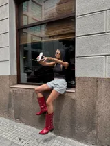 Bota estilo biker de caña alta, confeccionada en cuero vacuno color rojo cherry. Presenta un diseño con múltiples tiras horizontales con hebillas metálicas, punta redondeada y taco cuadrado bajo de madera.