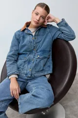 Campera de jean en tono azul medio, con cuello de pana en color marrón, cierre frontal con botones metálicos y bolsillos frontales tipo cargo.