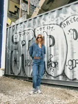 Chaleco de jean azul con cuello en V, cierre frontal con botones metálicos, bolsillos delanteros y corte a la cintura.