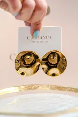 Caravanas circulares de diseño minimalista con superficie texturizada y acabado brillante. Presentan una forma ligeramente cóncava que refleja la luz, aportando un toque moderno y elegante.