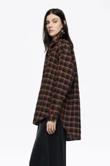 Camisa de corte recto y largo medio, confeccionada en tejido de algodón con textura. Presenta un diseño de cuadros en tonos rojo, negro y azul, cuello camisero, cierre frontal con botones, manga larga con puños abotonados y bolsillo de plastrón en el pecho.