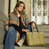 Poncho abierto de tejido de punto con diseño de rayas horizontales multicolor y patrones geométricos. Presenta terminaciones con flecos en el ruedo.
