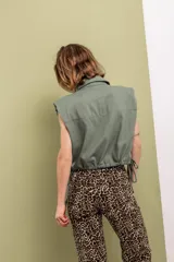Camisa sin mangas color verde oliva, con cuello clásico, cierre frontal con botones, hombreras y cintura ajustable con cordones.