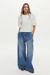Blusa blanca con cuerpo de jersey y mangas de tela plana abullonadas. Cuenta con volados en los hombros decorados con bordados en contraste.